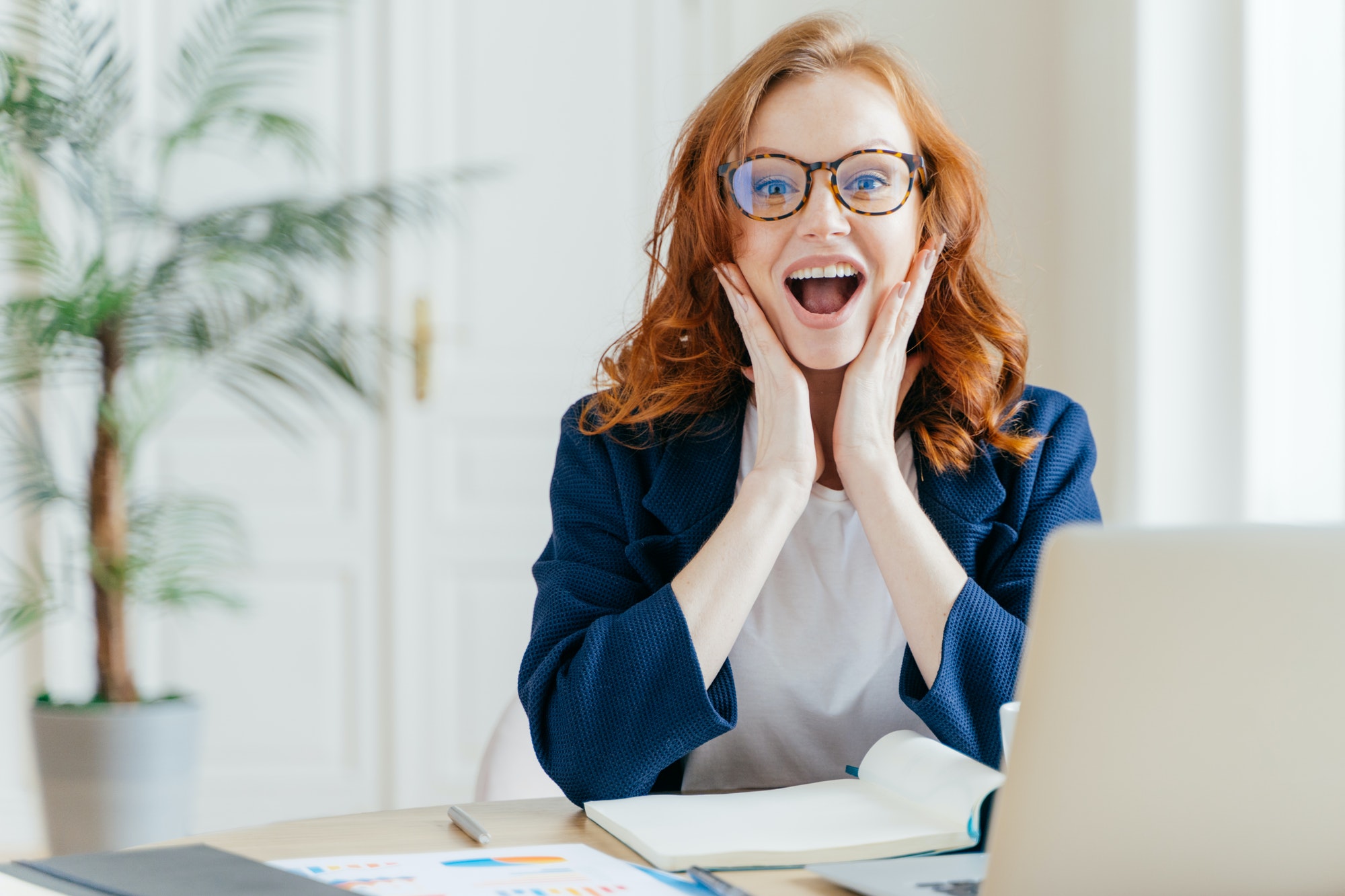 Female office worker looks at camera, rejoices promotion and receiving money reward for good work